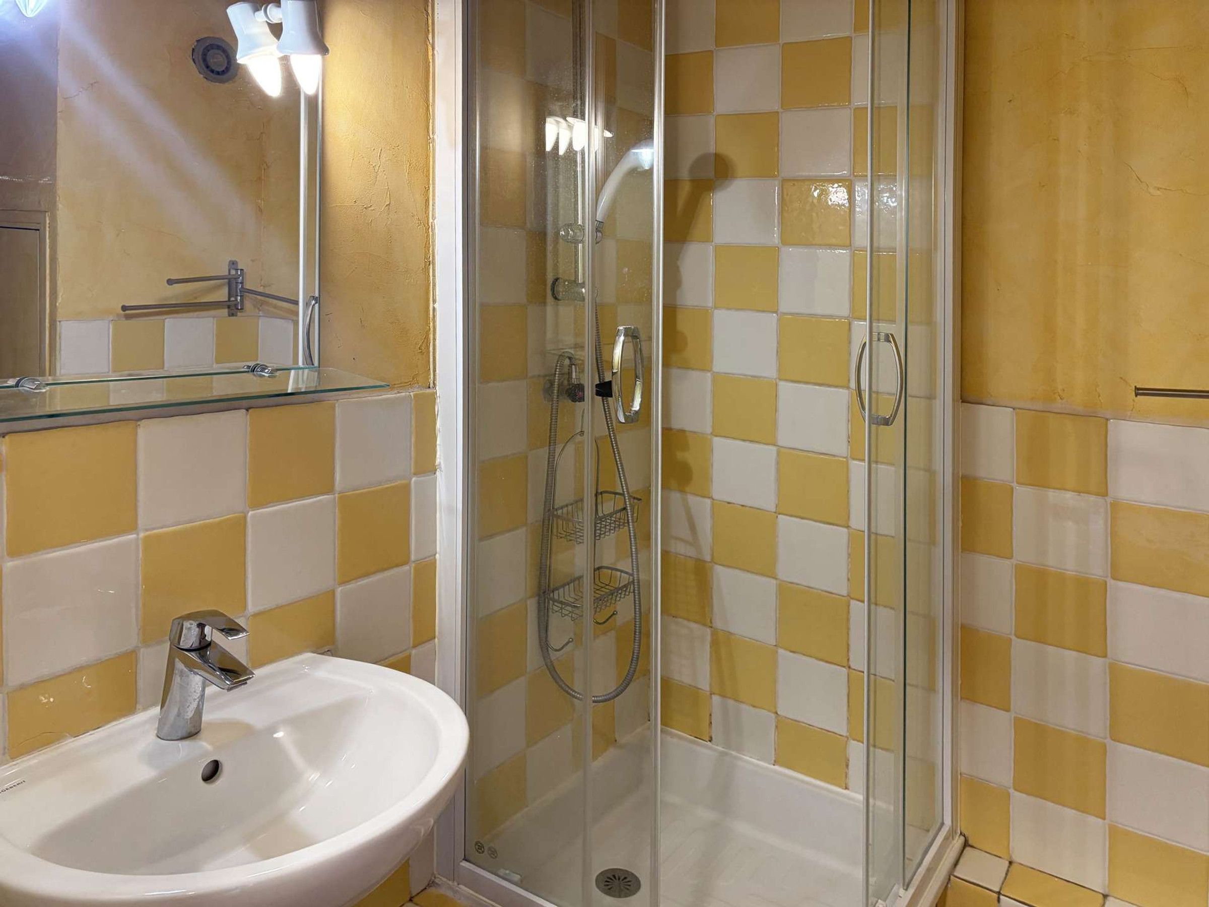 A bathroom with a glass-enclosed shower, a white sink, and yellow and white checkered tiles.