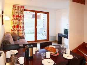 Uma área de refeições com mesa posta para o café da manhã, um sofá, uma televisão e vista para o exterior.