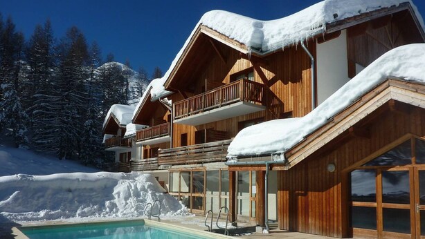 A wooden chalet with a pool, surrounded by snow-covered trees and mountains. - Spacious Chalet for 10 with Fireplace, Ski-In/Ski-Out, Pool, Sauna & Parking (Les Orres)