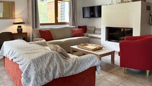 A cozy living room with a red sofa, a wooden coffee table, and a fireplace. - Spacious Chalet for 10 with Fireplace, Ski-In/Ski-Out, Pool, Sauna & Parking (Les Orres)