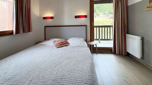 A bedroom with a large bed, two bedside lamps, a small table, and a view of a balcony. - Spacious Chalet for 10 with Fireplace, Ski-In/Ski-Out, Pool, Sauna & Parking (Les Orres)