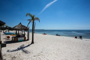 A beach with a thatched-roof hut, a jet ski rental sign, and a clear blue sky. - 555 Little Harbor (Ruskin)