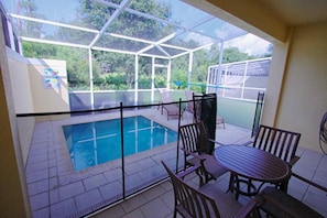 A covered outdoor area with a pool, patio furniture, and a glass enclosure.