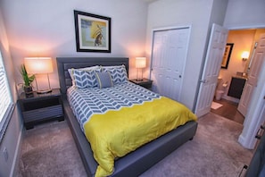 A bedroom with a bed, nightstands, a lamp, a door, and a hallway.