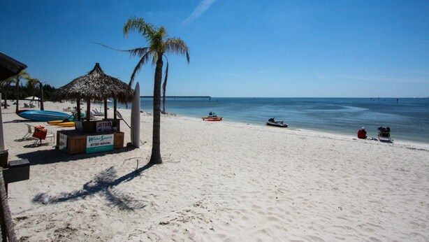Une plage avec un abri à toit de chaume, une pancarte indiquant la location de jet-skis et un ciel bleu dégagé.