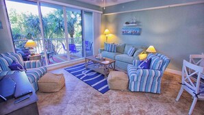 Un salon comprenant un canapé, un pouf et des fauteuils, une table basse, ainsi qu’un balcon avec des chaises et une table.