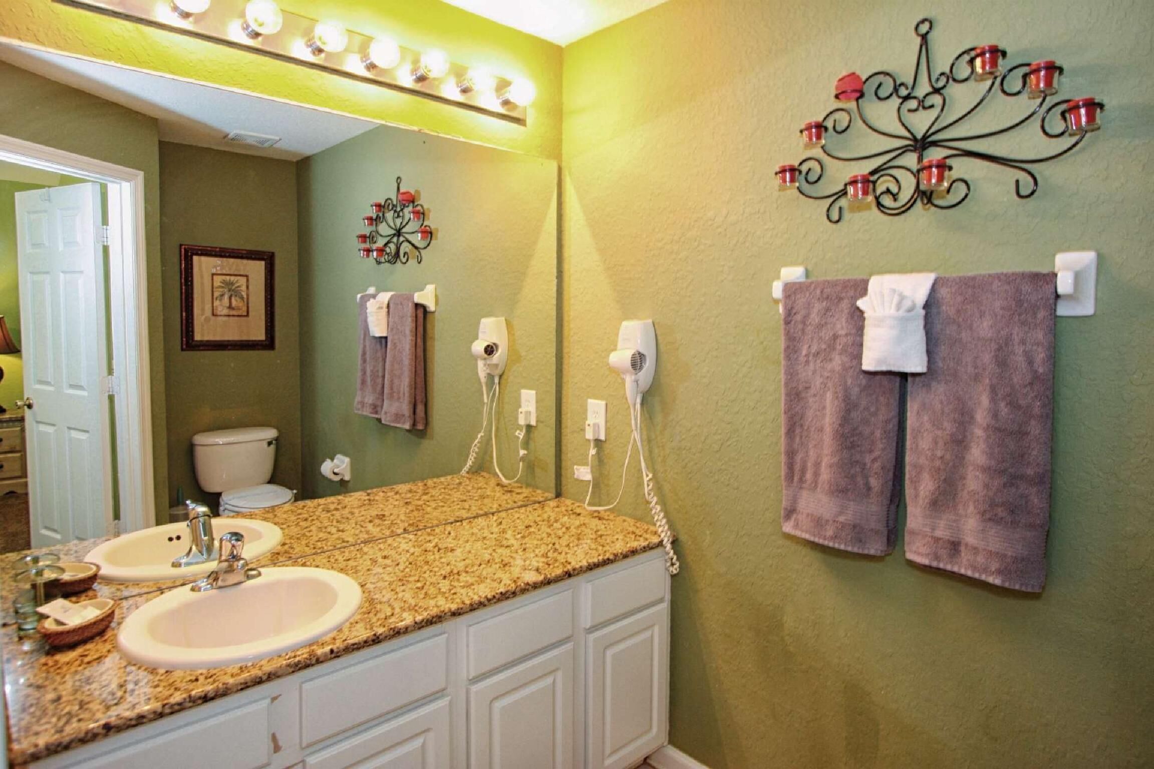 A bathroom with two sinks, a vanity, a towel rack with towels, a toilet, and a decorative wall piece.