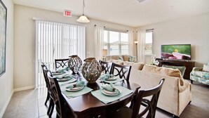 A dining area with a table set for four, a sofa, and a television in a living room. - 5131 Compass Bay (Kissimmee)