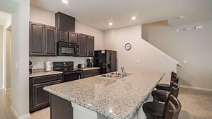 A modern kitchen with dark wood cabinets, a granite countertop, stainless steel appliances, and a built-in island with bar seating. - 5131 Compass Bay (Kissimmee)