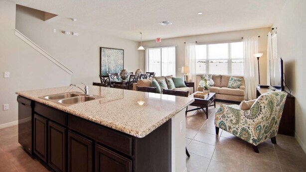A modern kitchen with a central island, dark cabinetry, and a dining area with a sofa and chairs. - 5131 Compass Bay (Kissimmee)
