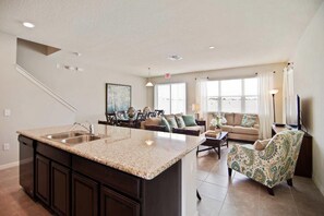 A modern kitchen with a central island, dark cabinetry, and a dining area with a sofa and chairs. - 5131 Compass Bay (Kissimmee)