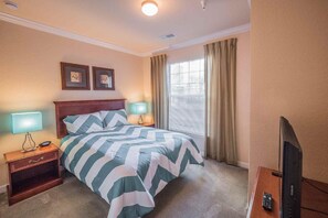 A hotel room with a bed, two bedside lamps, a television, and a window with curtains.