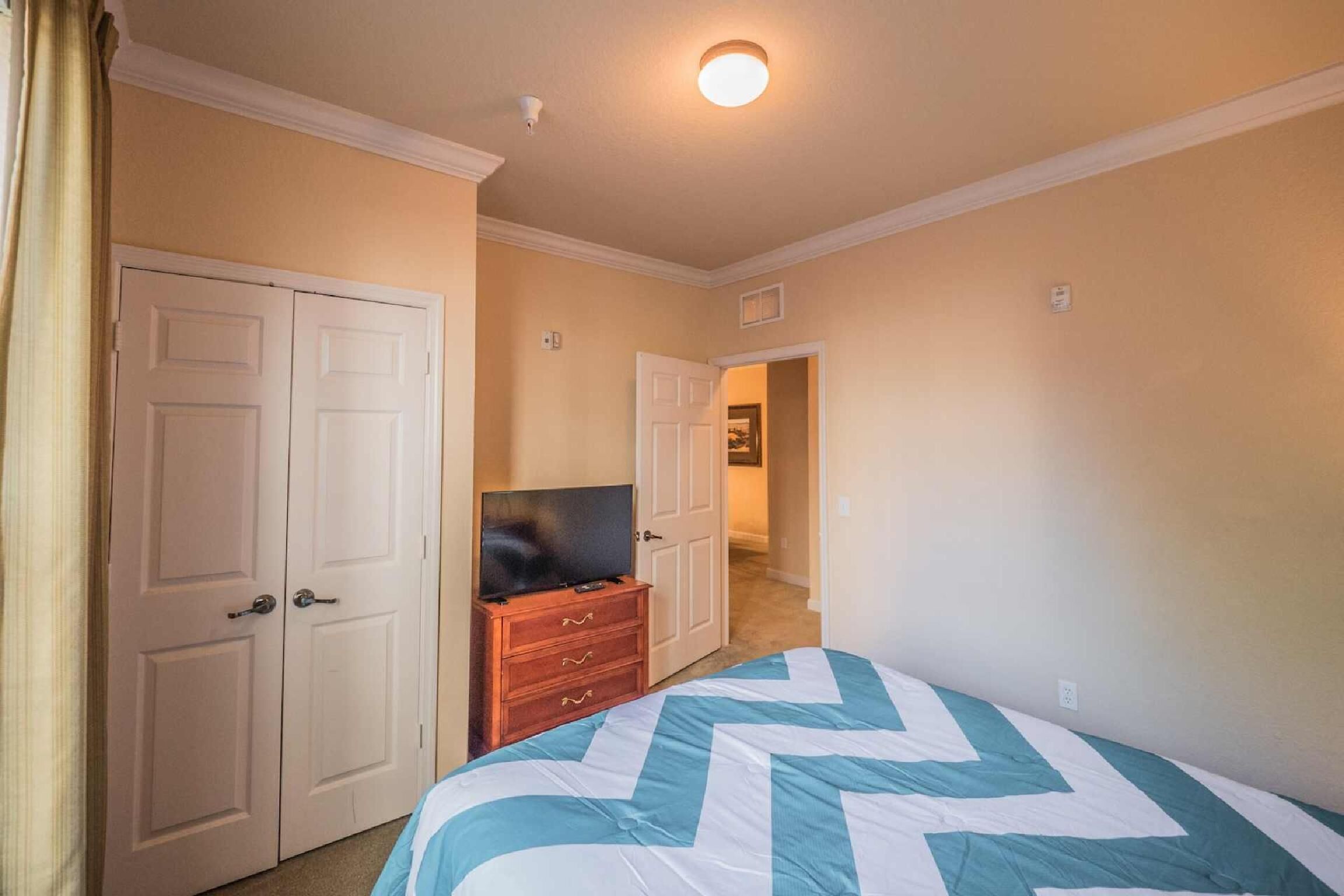 A bedroom with a bed, a TV on a dresser, and two doors leading to other rooms.