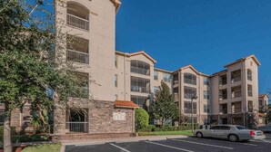 A multi-story residential building with balconies, a parking lot, and a clear blue sky. - 1361 Tuscana (Davenport)