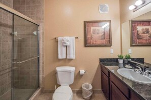 A bathroom with a glass-enclosed shower, a toilet, a sink with a mirror, and two framed pictures on the wall.