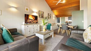 A modern living room with leather sofas, a coffee table, and a fireplace. There is a dining area with a table and chairs, and a kitchen in the background.