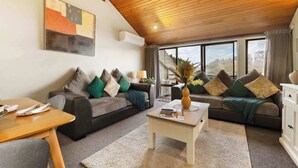 A cozy living room with a wooden ceiling, two sofas with cushions, a coffee table, and a dining table with cutlery.