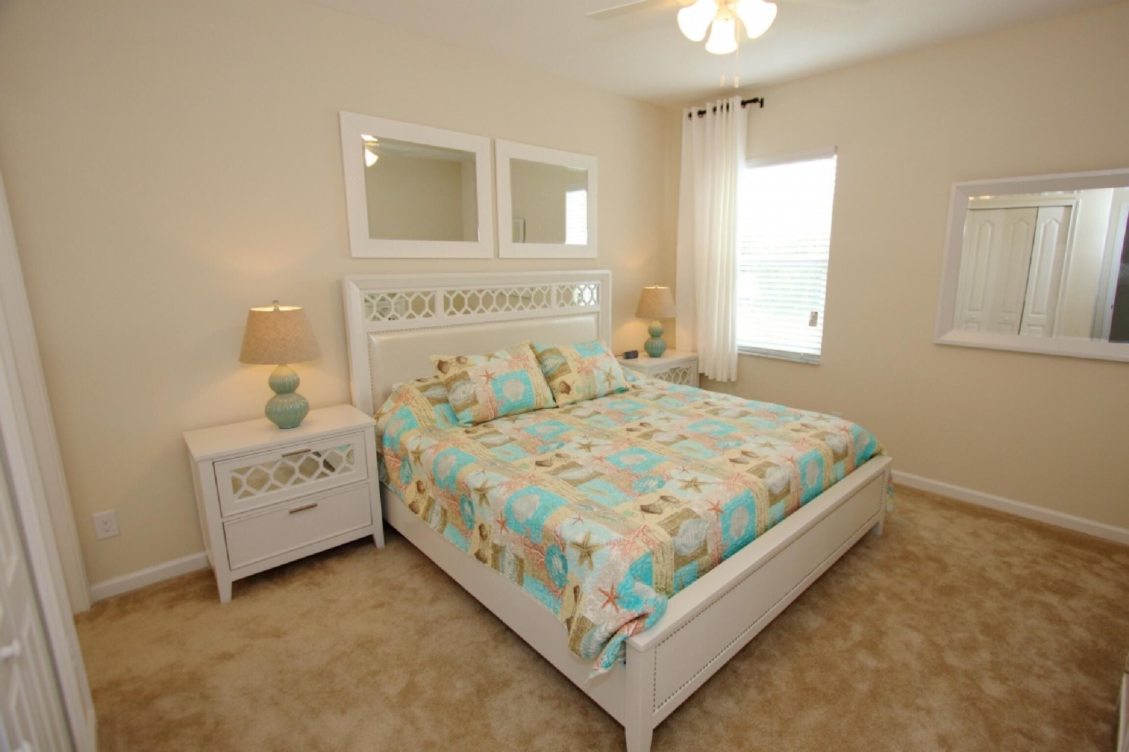 A bedroom with a bed, nightstands, a ceiling fan, and a window with curtains.