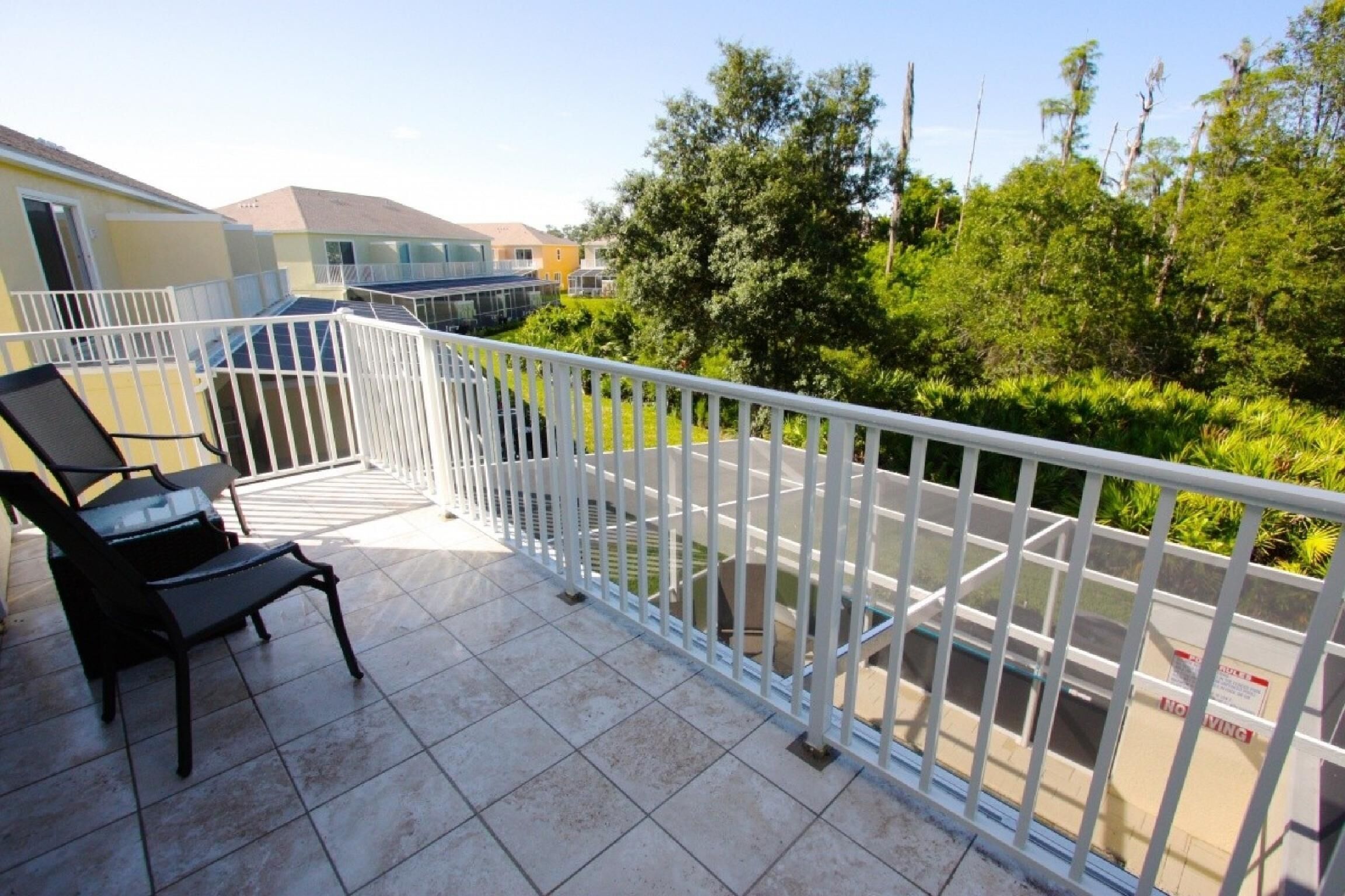 Un balcon avec une balustrade blanche, une chaise noire et une vue sur un paysage verdoyant et des bâtiments.