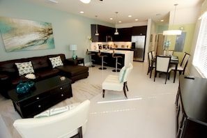 A modern living room with a sofa, ottoman, and coffee table, a dining area with chairs and a table, and a kitchen with bar stools. - 1533 Dream (Clermont)
