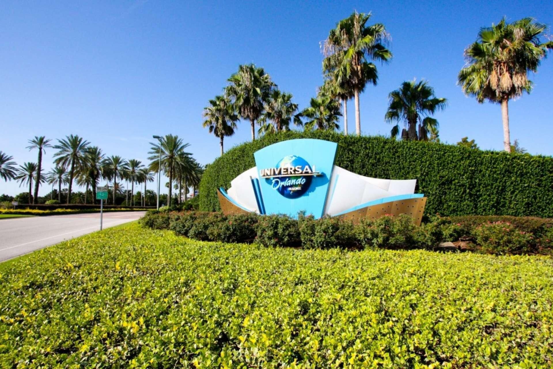Une enseigne pour Universal Orlando, au design incurvé, entourée d’une végétation luxuriante et de palmiers.