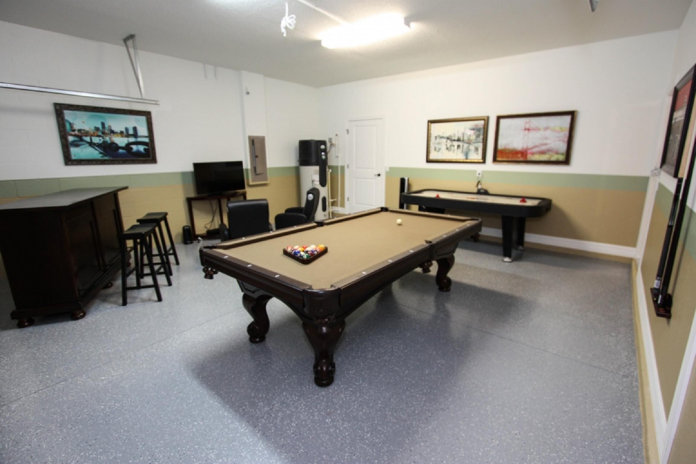 A pool table with a pool cue and balls, a television, and a cabinet in a room with a tiled floor and green and beige walls.