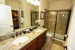 A bathroom with a double sink vanity, a large mirror, and a glass-enclosed shower area. - 1484 Champions Gate (Davenport)