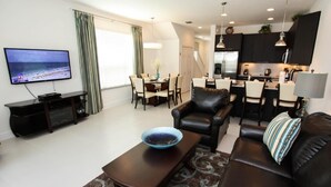A modern living room with a flat-screen TV, a dining area, a kitchen, and a cozy seating area. - 17521 Dream (Clermont)
