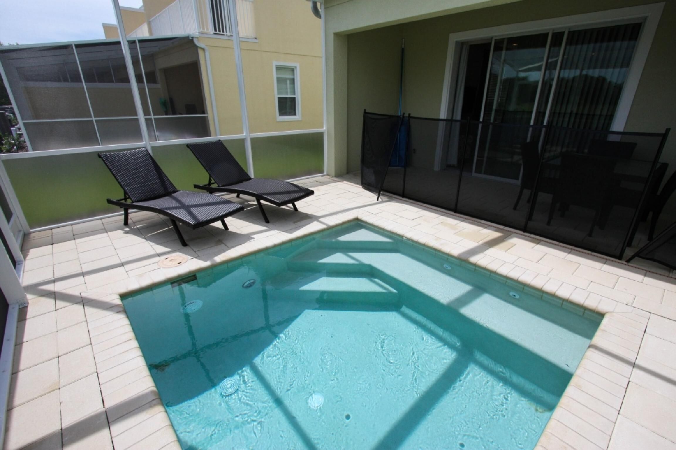 A swimming pool with two lounge chairs, a covered patio area, and a sliding glass door.