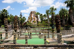 A fenced area with rope bridges, stone structures, and palm trees.