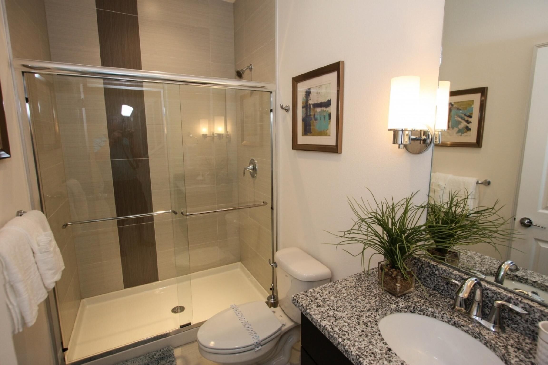 Une salle de bain dotée d’une douche à parois de verre, de toilettes, d’un lavabo avec un plan de travail en granit et de deux appliques murales.