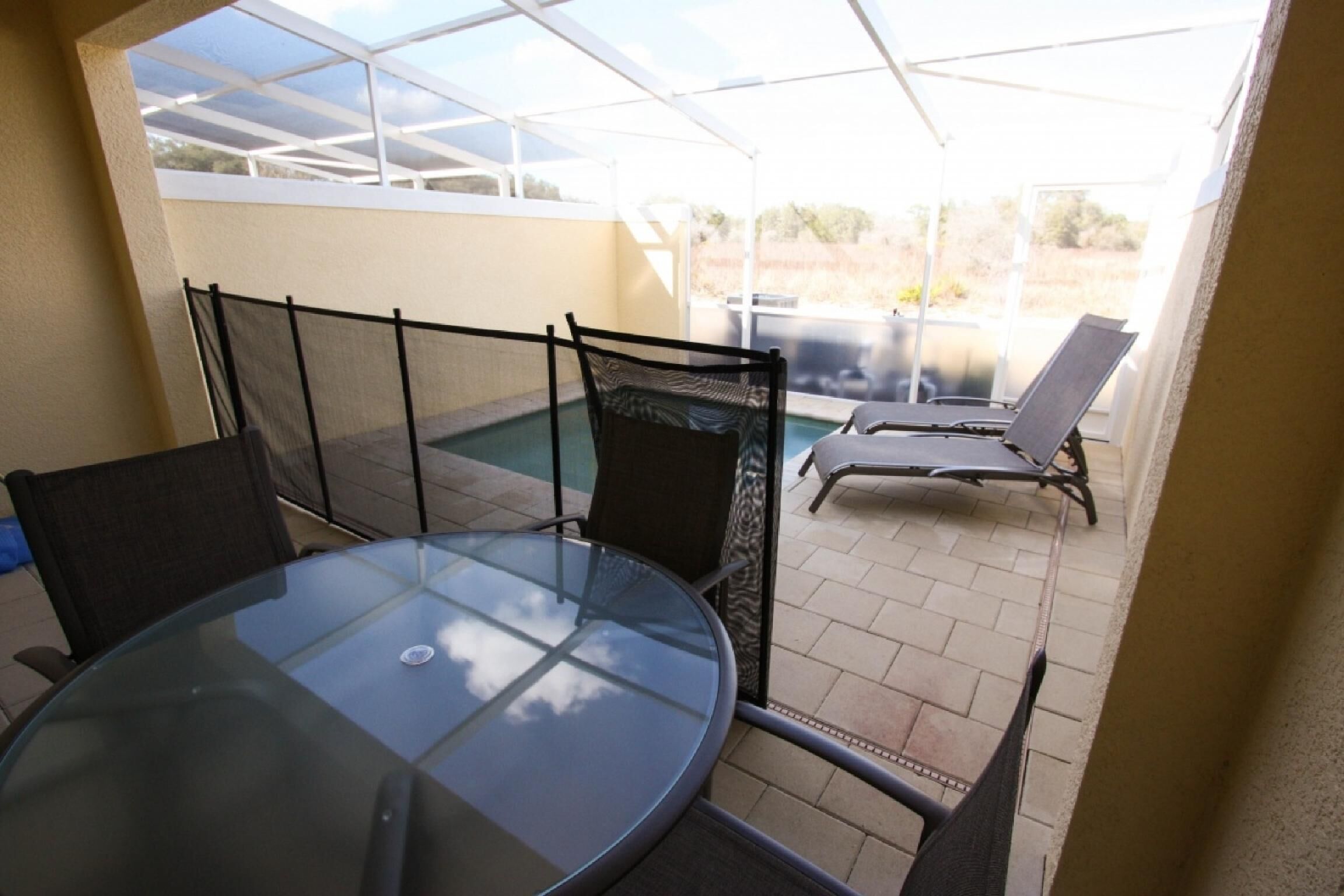 Eine verglaste Terrasse mit rundem Tisch und Stühlen, einem Pool und einer überdachten Sitzgruppe.