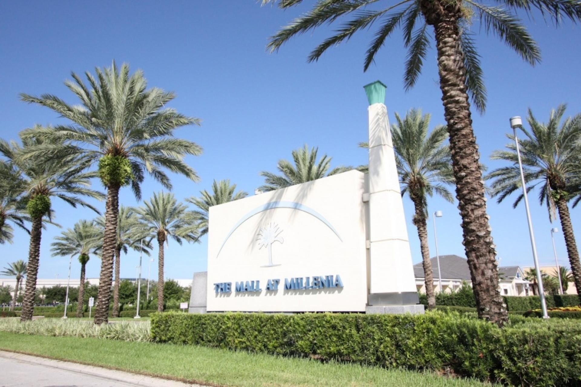 A sign for 'The Mall at Millenia' with a modern design, surrounded by palm trees and a clear sky.