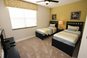A bedroom with two beds, a ceiling fan, a nightstand with a lamp, a desk with a computer, and a window with blinds. - 17531 Dream (Clermont)