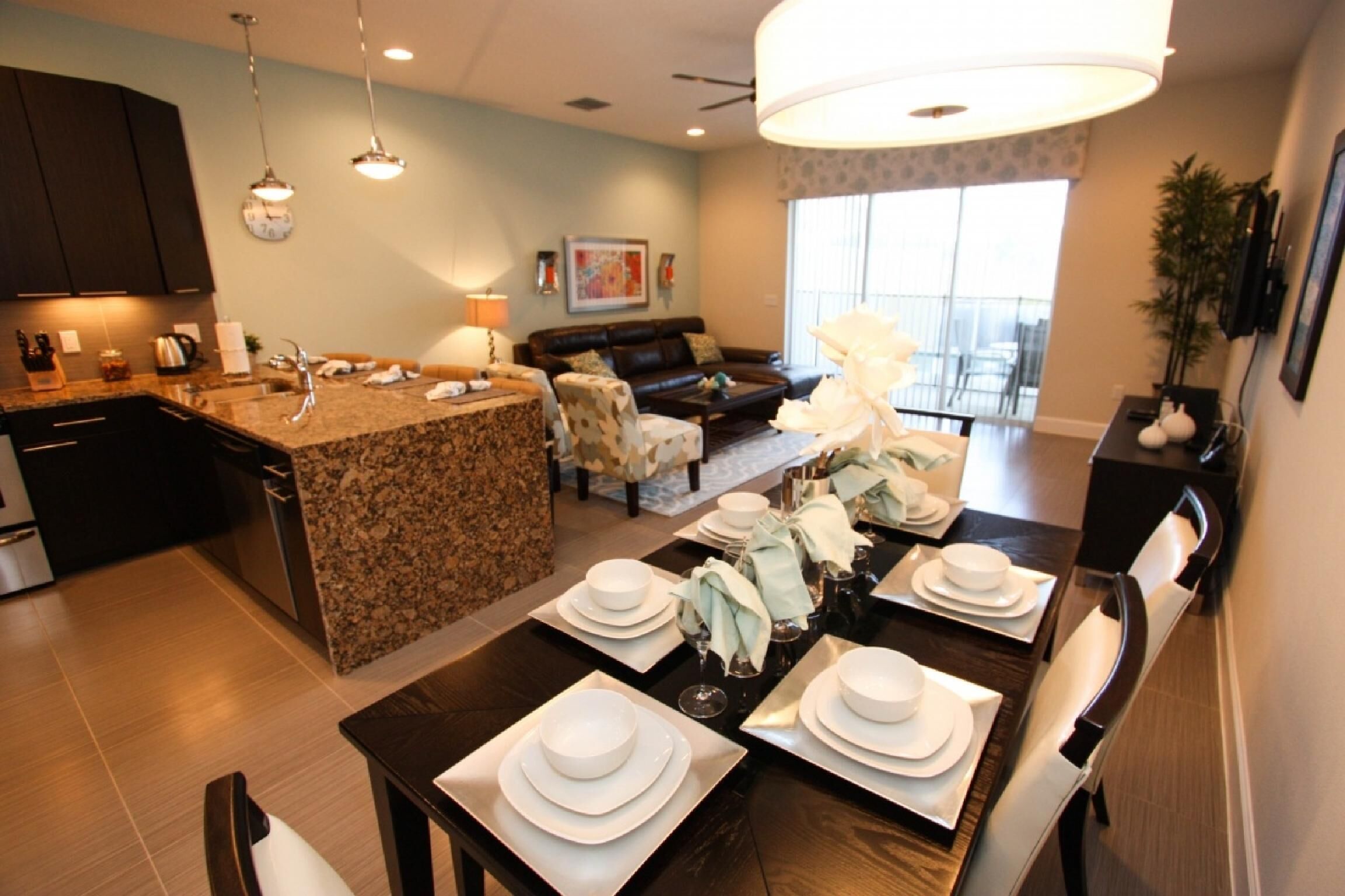 Una cocina moderna con encimeras de granito, una zona de comedor con mesa de madera preparada para cuatro comensales y una sala de estar con sofá y una mesa de centro.