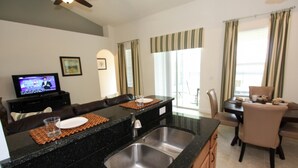 A modern kitchen with a granite countertop, stainless steel sink, and a dining area with a table and chairs. - 4072 Solterra (Davenport)