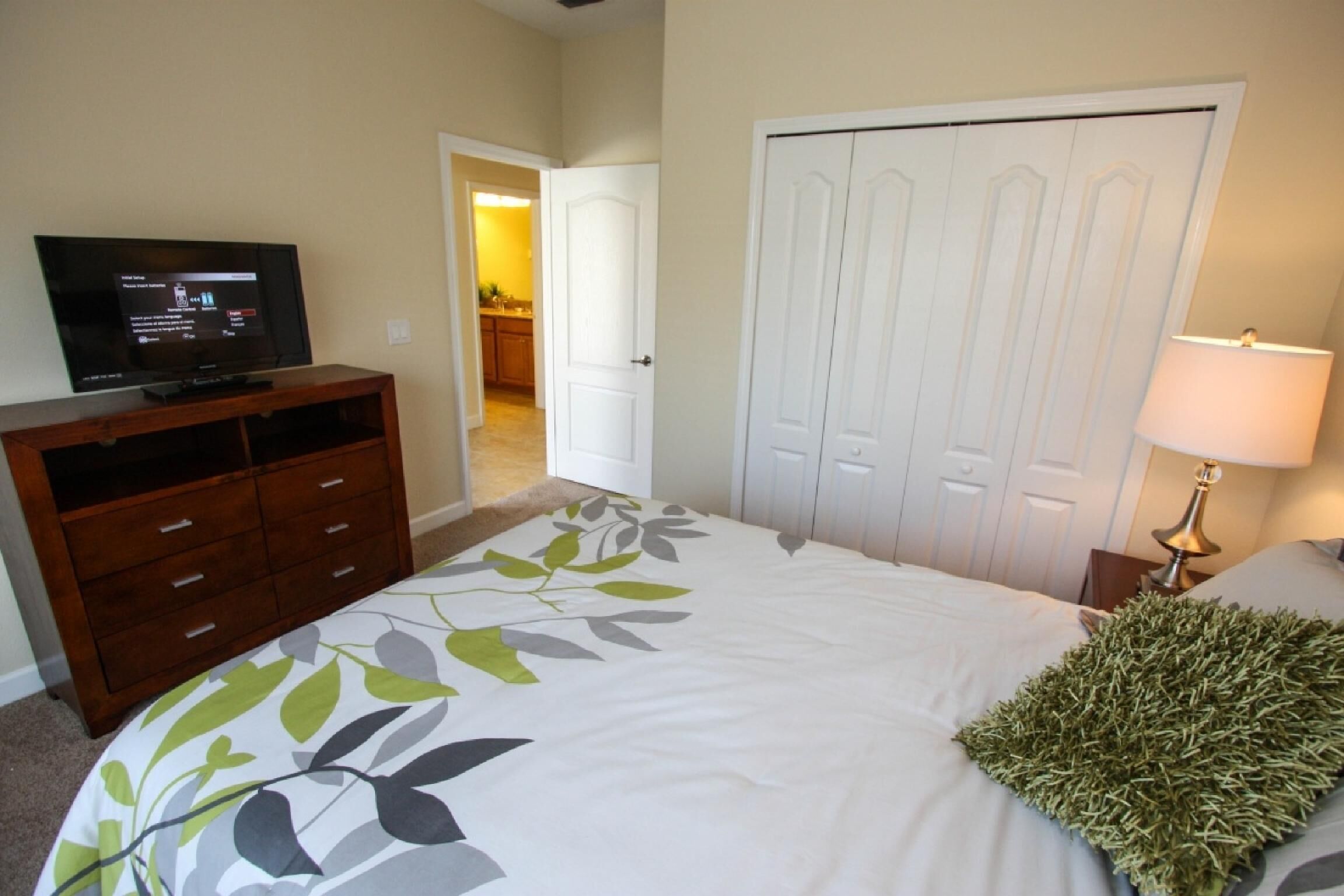 A bedroom with a bed, a dresser, a television, a door, and a lamp.