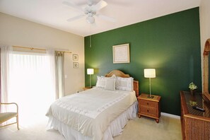 Ein Schlafzimmer mit Bett, Nachttischen, einem Sessel, einem Deckenventilator und einer grünen Wand.