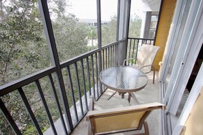 Ein Balkon mit Glastisch und zwei Stühlen, mit Blick auf eine Wohngegend mit Bäumen und Häusern.