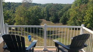 A deck with two Adirondack chairs and a white railing overlooking a forested landscape. - Ski In/Ski Out Mountain Top Condo at Crystal Mountain (Thompsonville)
