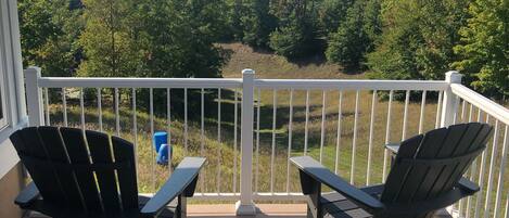 A deck with two Adirondack chairs and a white railing overlooking a forested landscape.