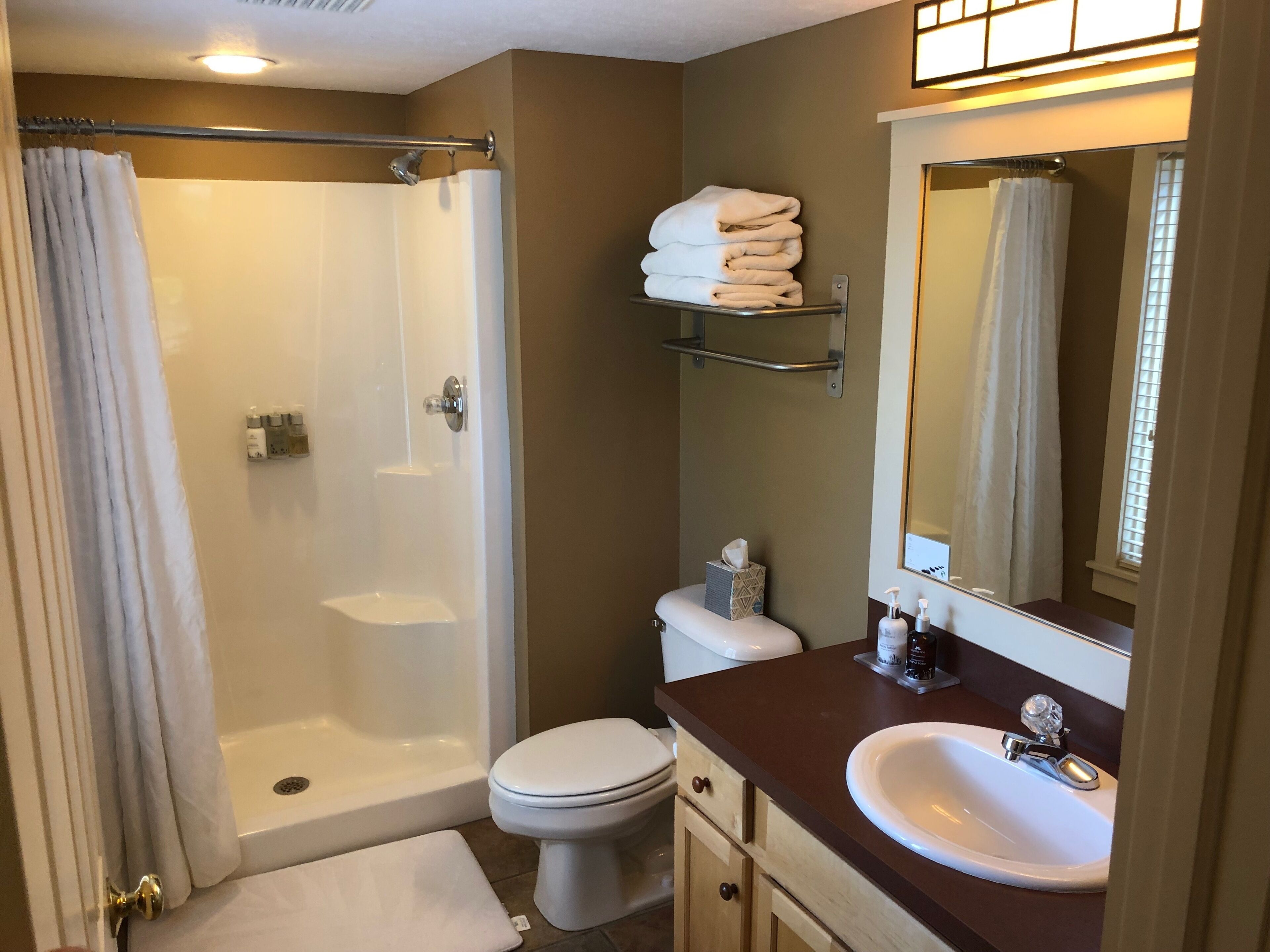 A bathroom with a shower, toilet, sink, and a towel rack with folded towels.