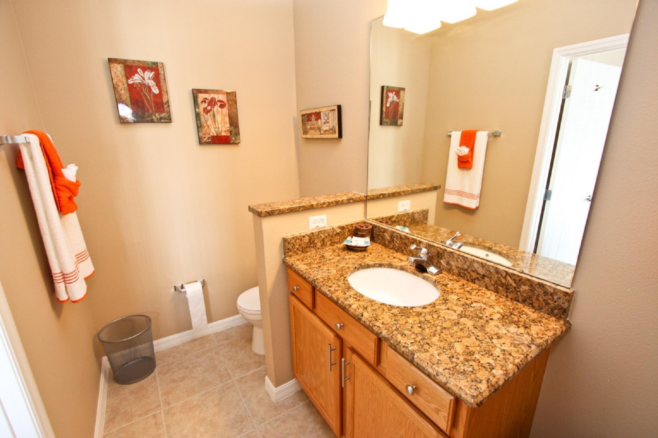 A bathroom with a granite countertop sink, wooden cabinets, a mirror, and two framed pictures on the wall.