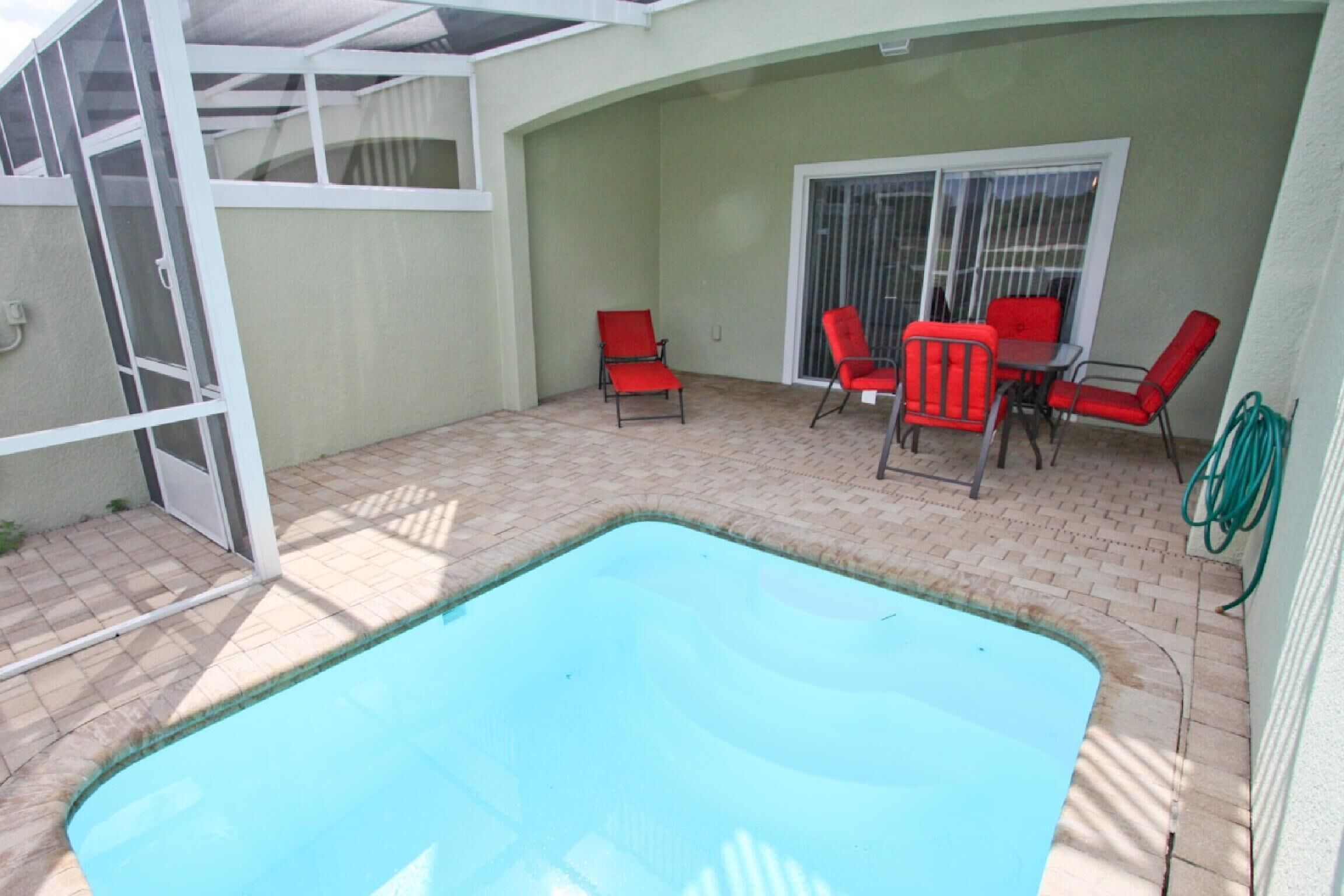 A swimming pool with red chairs and a table, surrounded by a covered patio area.