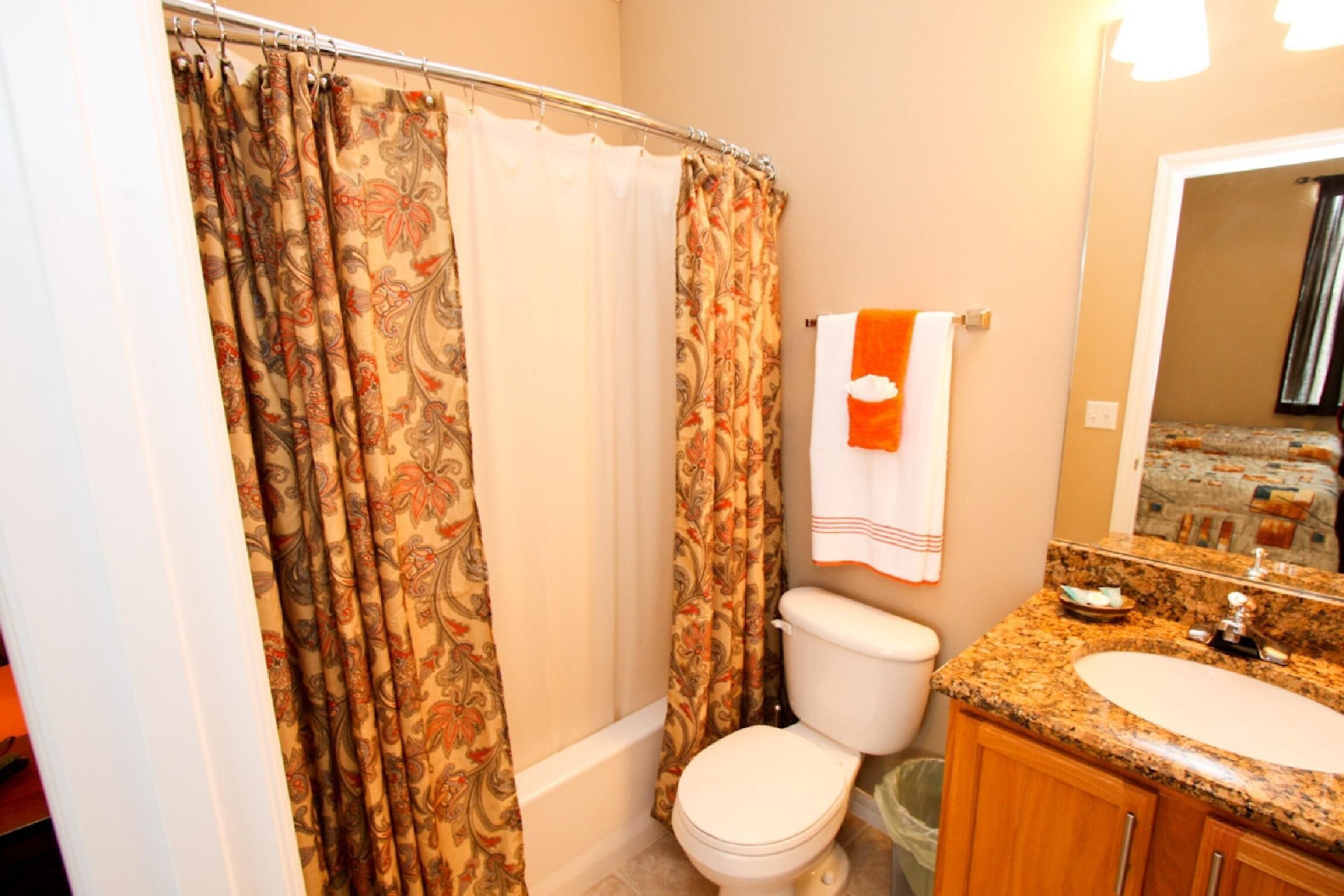 A bathroom with a shower curtain, toilet, sink, and mirror.