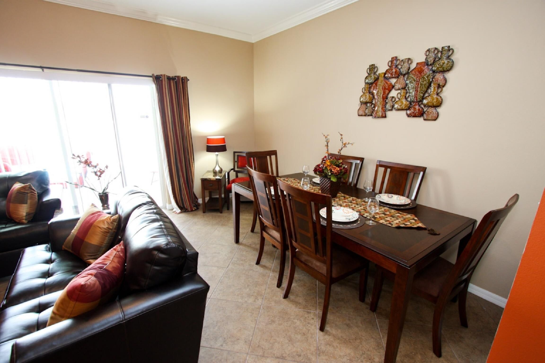 A dining area with a wooden table, chairs, and a chandelier. There is a sofa with cushions in the foreground.