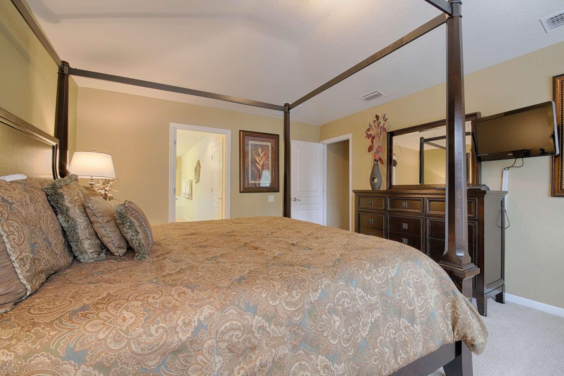 Un lit à baldaquin avec une couvre-lit à motifs, une commode avec un miroir et une porte donnant sur une autre pièce.