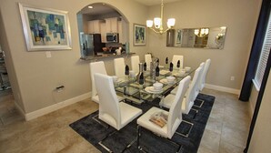 A dining area with a glass table, white chairs, and a chandelier. - 4201 Solterra (Davenport)