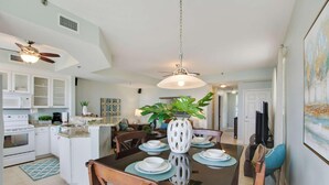 Una cocina moderna con armarios blancos, una isla central y un comedor con mesa y sillas de vidrio.