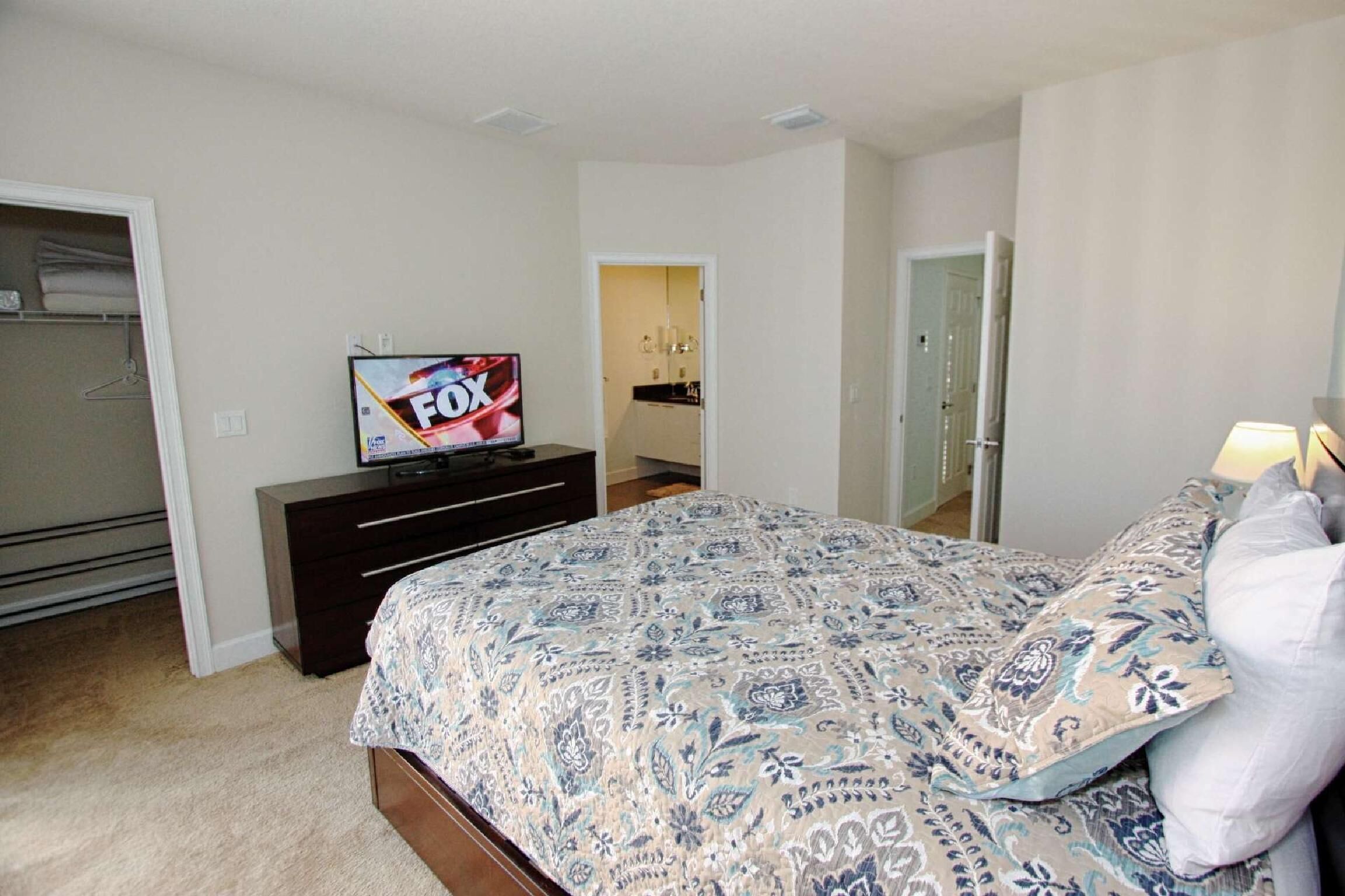 A bedroom with a bed, a dresser, a TV on the dresser, and a door leading to another room.